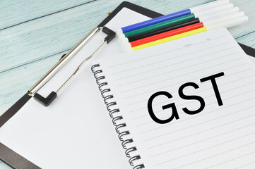 Top angle view of pen colors, paper holding file and notebook written with text GST on a wooden background. Business concept.