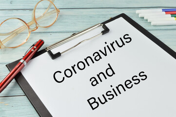 Selective focus of glasses, pen, colors and paper holding file written with text CORONAVIRUS AND BUSINESS. Business concept.