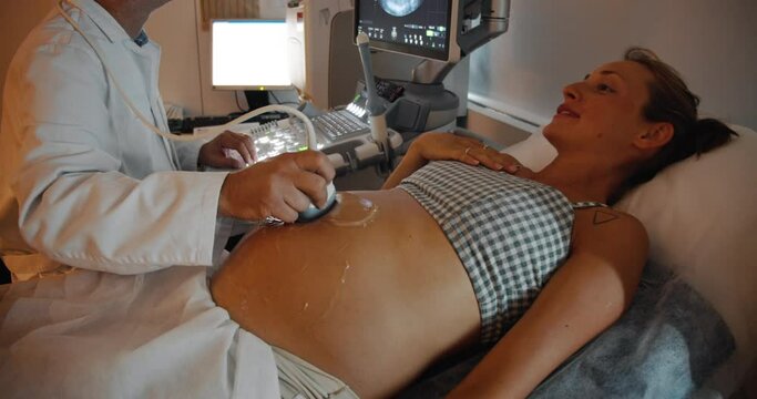 Happy pregnant woman lying down getting ultrasound investigation. Doctor fertility specialist uses ultrasound equipment while checking pregnant woman. Prenatal testing with ultrasound