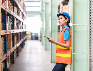 Asian female worker with safety vest and helmet working and using tablet pc computer in automotive spare parts warehouse