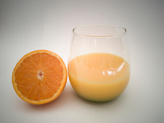 A glass goblet with orange juice. Juicy vibrant colorful oranges. Orange cut in half