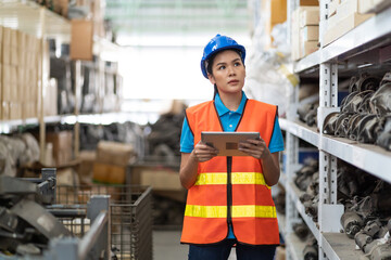 Asian female warehouse worker in safety vest and helmet working with tablet pc computer for...