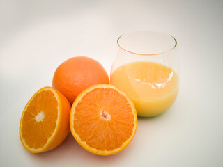 A glass goblet with orange juice. Juicy vibrant colorful oranges. Orange cut in half