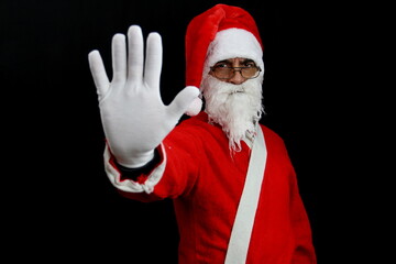 Santa claus on black background with serious face raises his arm and makes the stop sign with his hand. Christmas concept