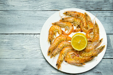 Cooked Fresh White Tiger Prawns with Lemon on a White Plate. Tarlka with seafood on a wooden table with lemon. Delicious food.