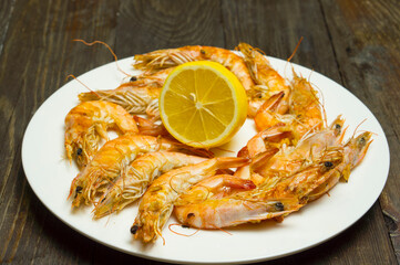Cooked Fresh White Tiger Prawns with Lemon on a White Plate. Tarlka with seafood on a wooden table with lemon. Delicious food.