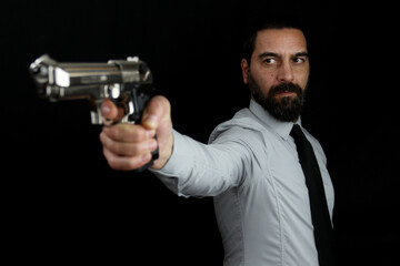 A handsome bearded man on black background holds a gun in his hand pointing it in front of him. Gangster, policeman