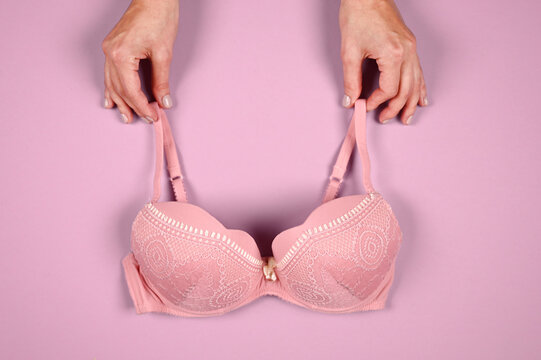 Female hands on a violet background holding a beautiful pink bra. Daily underwear concept. Sales concept.