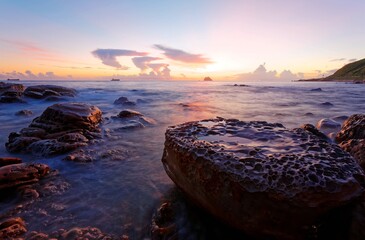 Beautiful sunrise scenery of a rocky beach on northern coast of Taiwan with an island on distant horizon & peculiar rock formations on seashore under dramatic dawning sky (Long Exposure Effect)