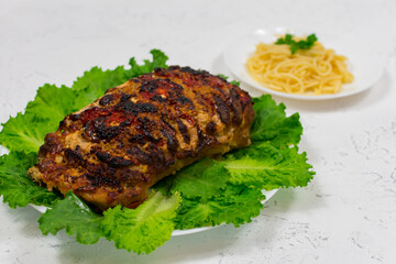 A large piece of chopped pork meat, cooked in the oven, baked in the oven, on green lettuce leaves, close-up.