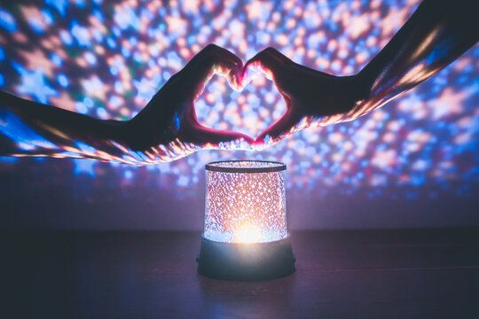 Cropped Hand Making Heart Shape Over Illuminated Lighting Equipment