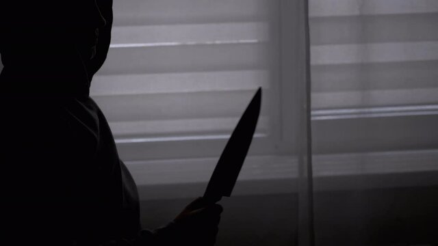 Silhouette of Lonely Child in Hood with Knife in Hand near Window. Killer Teen