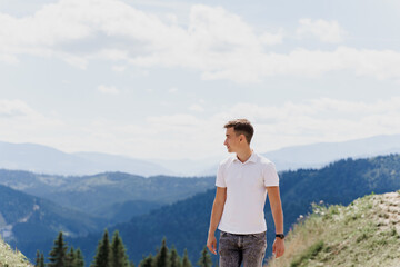 Fototapeta premium Men traveler is smiling and posing on the green hills background. Advert for travel agency. Tourism. Travelling in the mountains.