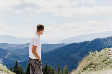 Naklejka premium Men traveler is smiling and posing on the green hills background. Advert for travel agency. Tourism. Travelling in the mountains.