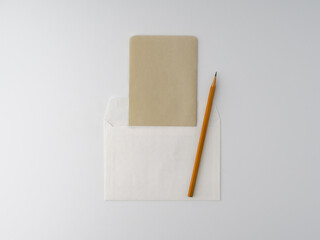 An empty kraft brown card for an invitation or greeting, a white paper envelope, and a yellow pencil on a white background. Layout. Stylized stock photos. The view from the top. Mock-up.