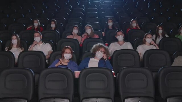 Multiracial audience wearing face masks enjoying time in cinema.