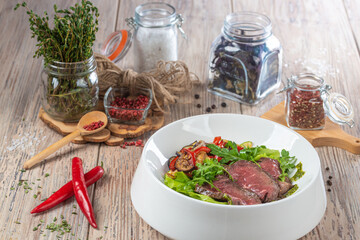 plate with fried cuts of meat and salad with arugula on wooden background, close view 