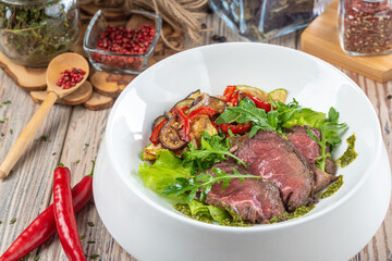 plate with fried cuts of meat and salad with arugula on wooden background, close view 
