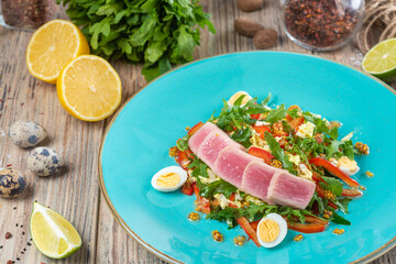 plate with salad of quail eggs and bell pepper with fish slices and arugula on wooden background, close view 