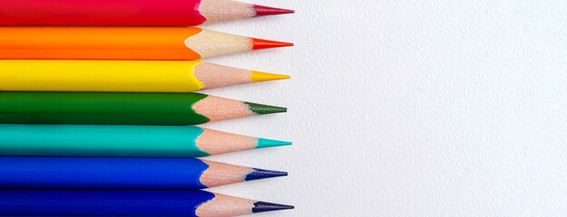 Banner with sharp coloured wooden pencils. Close-up. Colorful pencils on white paper. Creativity and education. Copy space. Top view.