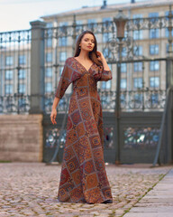 Elegant woman with longhair in brown dress walking at street in the city on a summer day