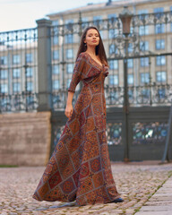 Elegant woman with longhair in brown dress walking at street in the city on a summer day