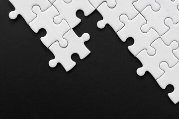 Unfinished white jigsaw puzzle pieces on black background with  copy space