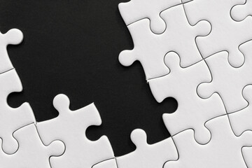 Unfinished white jigsaw puzzle pieces on black background