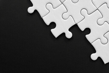 Fototapeta premium Unfinished white jigsaw puzzle pieces on black background with copy space