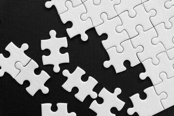 Unfinished white jigsaw puzzle pieces on black background