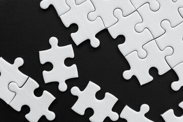 Fototapeta premium Unfinished white jigsaw puzzle pieces on black background
