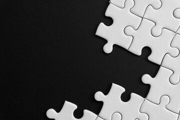 Obraz premium Unfinished white jigsaw puzzle pieces on black background with copy space