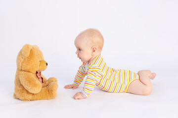 smiling baby girl 6 months old lies on a white isolated background in a bright bodysuit in front of a soft Teddy bear, space for text