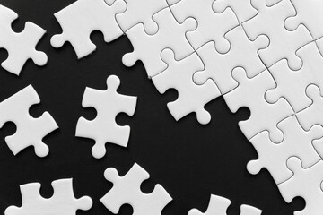 Unfinished white jigsaw puzzle pieces on black background