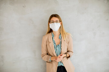 Young woman standning by the grey wall and wearing a respiratory mask from coronavirus disease