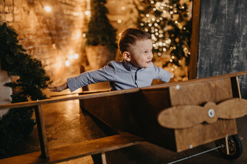 Child boy plays in toy plane against background of Christmas decorations.