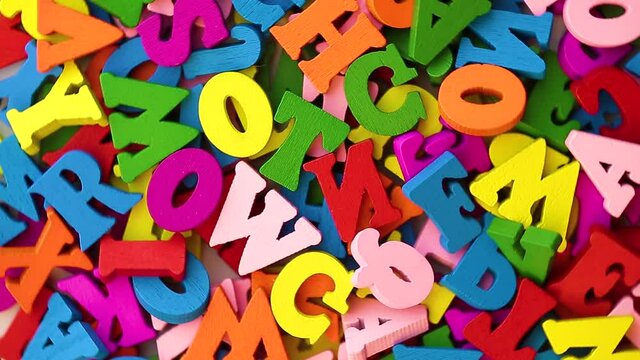 Multi-colored letters are scattered in a chaotic manner moving in a circular rotation, close-up top view, flat lay.
