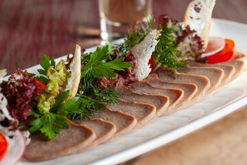 Delicious restaurant dish of thinly sliced boiled beef tongue with herbs on a large white plate with a selective focus.