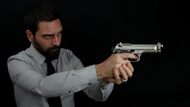 Handsome bearded man in shirt and tie on black background loads the shot in the barrel of his silver pistol and takes aim. Policeman dressed in civilian clothes