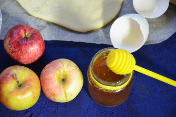 Various ingredients for winter seasonal baking and other recipes, honey, apples, herbs and spices on a dark blue background. Top view.
