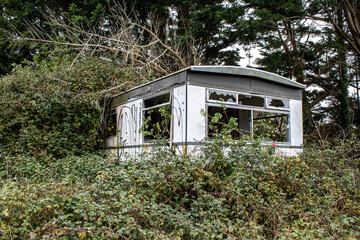 abandoned and broken mobile home trailer falling apart in the tall grass and forest.