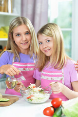 Obraz na płótnie Canvas Two girls in pink aprons preparing salad on kitchen table