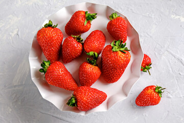A plate of beautiful strawberries isolated on grey concrete. Tasty and healthy diet. Top view.
