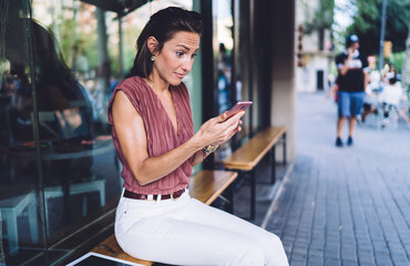 Expressive female brunette using smartphone for checking notification surprised with news from banking app, emotional caucasian woman stressed with losing money and trouble with online payment