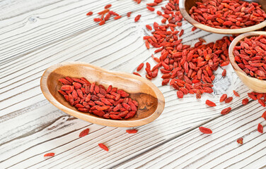 Dried goji aka. wolfberry seeds in wooden bowls and spilled on white boards desk