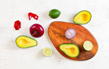Avocado halves, limes and onions - basic guacamole ingredients on white working board, flat lay photo