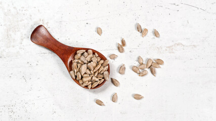 Peeled sunflower seeds in small wooden scoop, placed on white stone like board, view from above