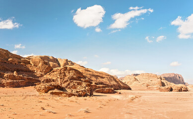 Fototapeta na wymiar Rocky massifs on red sand desert, vehicle tracks ground, bright cloudy sky in background, typical scenery in Wadi Rum, Jordan