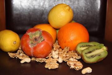 Colorful fruits and walnuts on a dark background. Persimmon, kiwi, citrus

