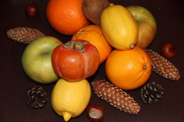 Bright colored fruits and walnuts, cones on a dark background. Persimmon, kiwi, citrus